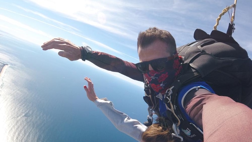 A man taking a selfie while tandem skydiving over the ocean.