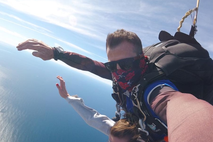 A man taking a selfie while tandem skydiving over the ocean.