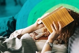 Women in bed with book over her face for story on whether you are too sick to go to work