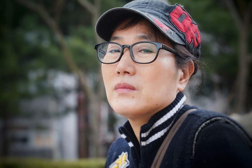 A Korean woman in glasses looking soulfully at the camera 