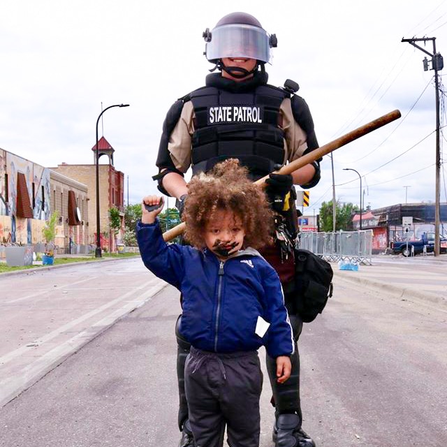 A little boy with his fist in the air standing in front of a smiling police officer