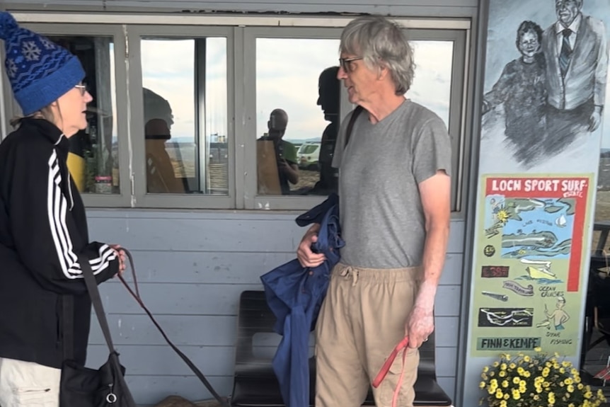 A man talks with a woman who is holding two dogs on a leash.