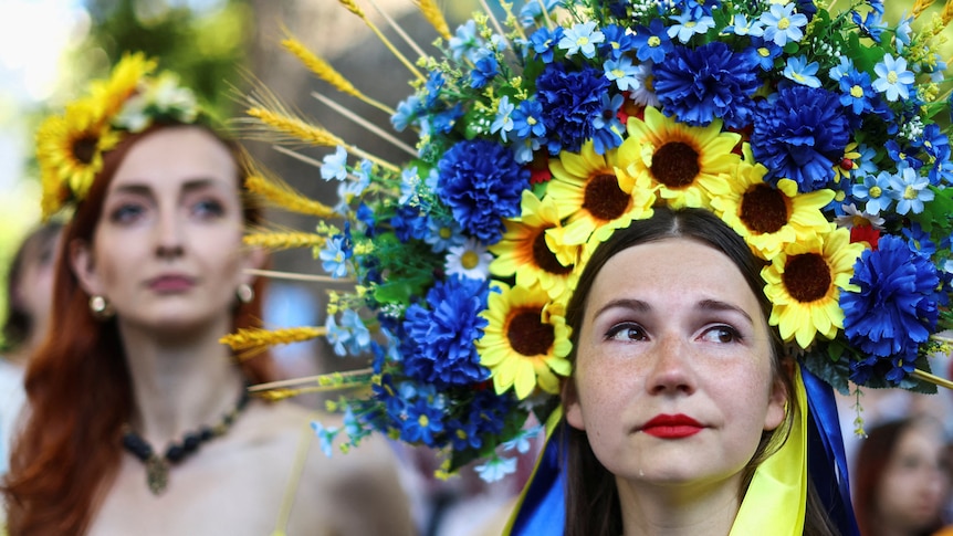 A woman in a blue and yellow floral headpiece cries.