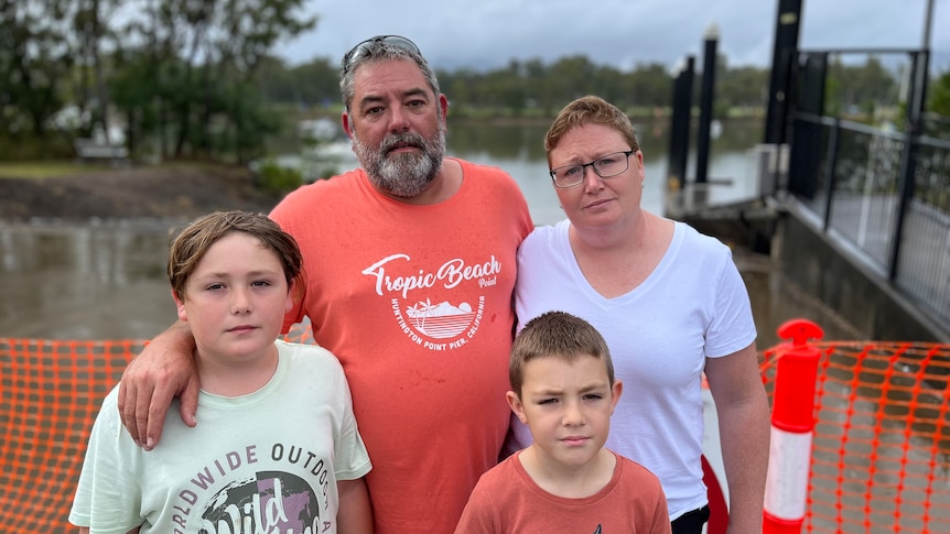 A mum, dad and two boys at a boat ramp looking sad.
