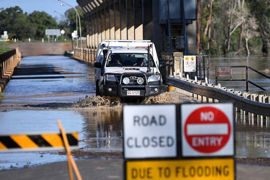 A four-wheel drive ute drives over a partially flooded river bridge