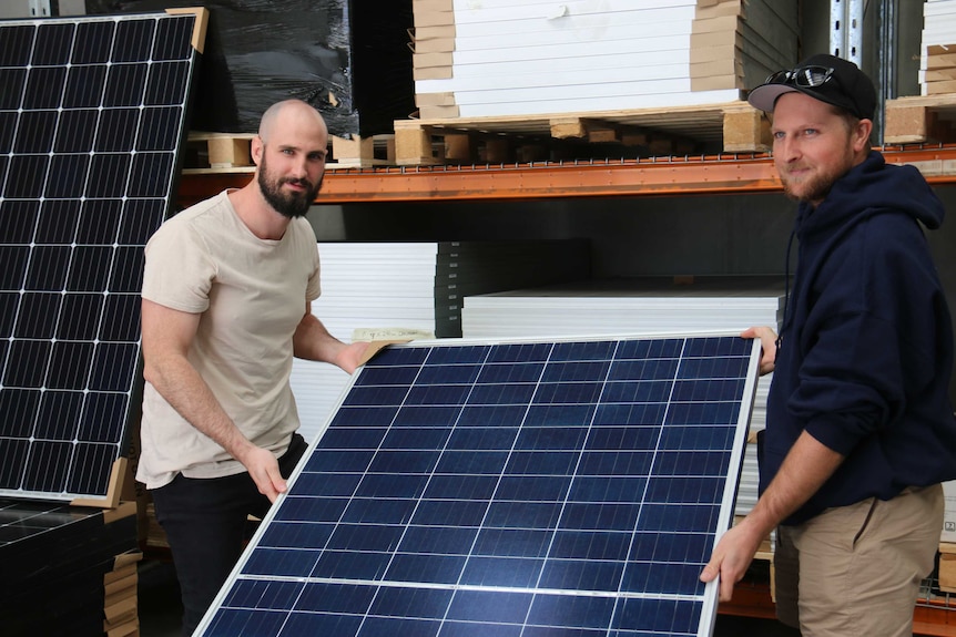 Sam Kent (left) holds a solar panel with one of his workers.