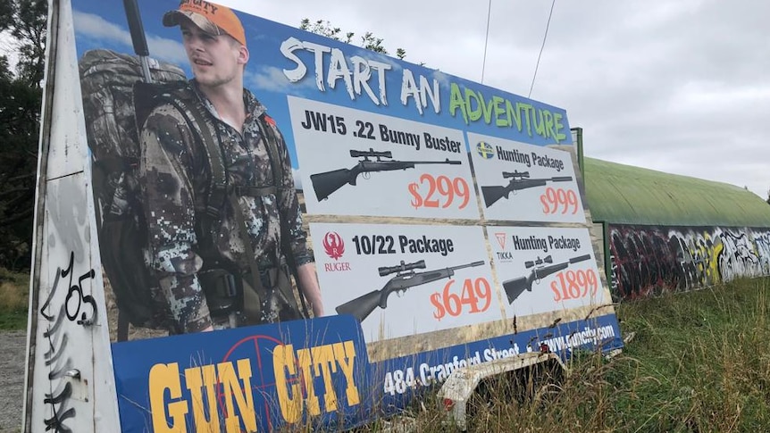 A long roadside billboard promoting the sale of guns, with the tagline 'start an adventure'