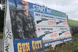 A long roadside billboard promoting the sale of guns, with the tagline 'start an adventure'