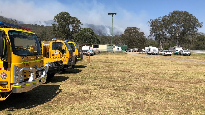 Three fire trucks line up at the showgrounds, with a fire burning in the background.
