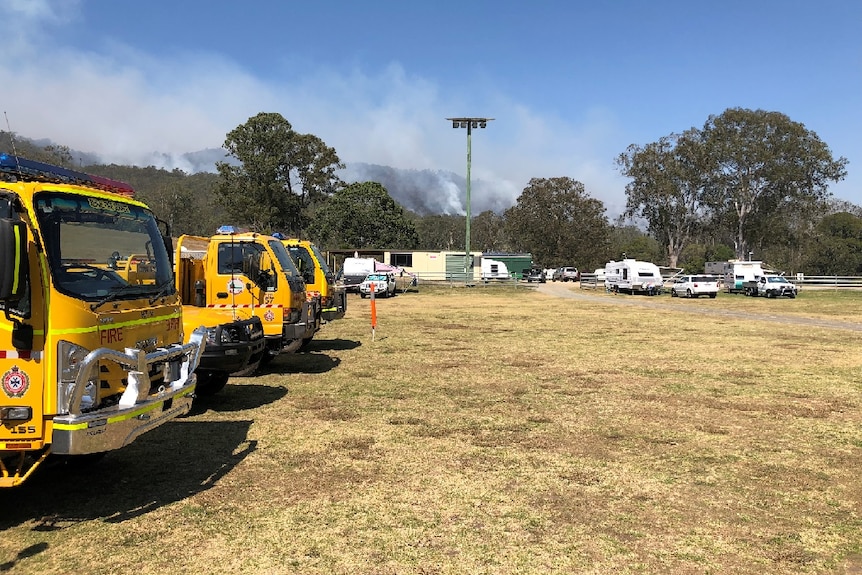 Three fire trucks line up at the showgrounds, with a fire burning in the background.