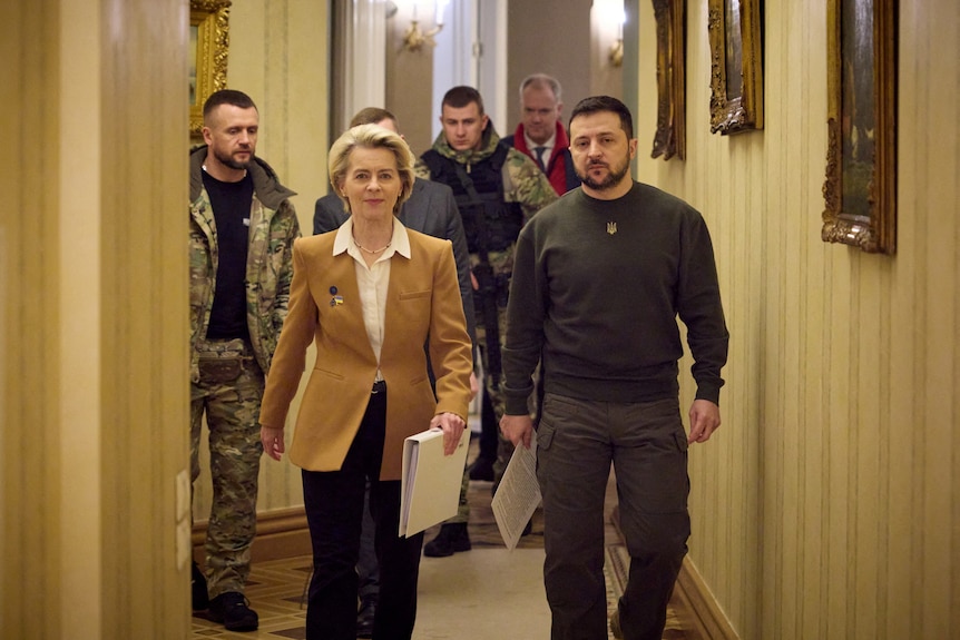 Ursula von der Leyen and Volodymyr Zelenskyy walk down hallway, followed by officials.