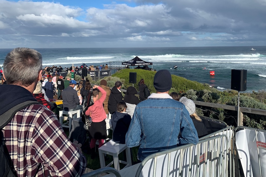 A crowd stands on the shore watching a surf break