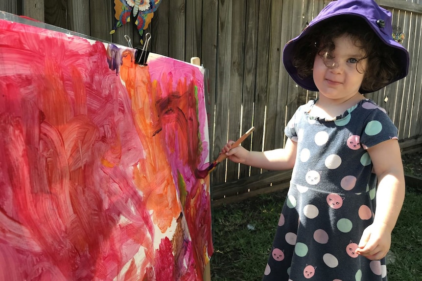 A four-year-old girl does a painting while outside at a daycare centre.