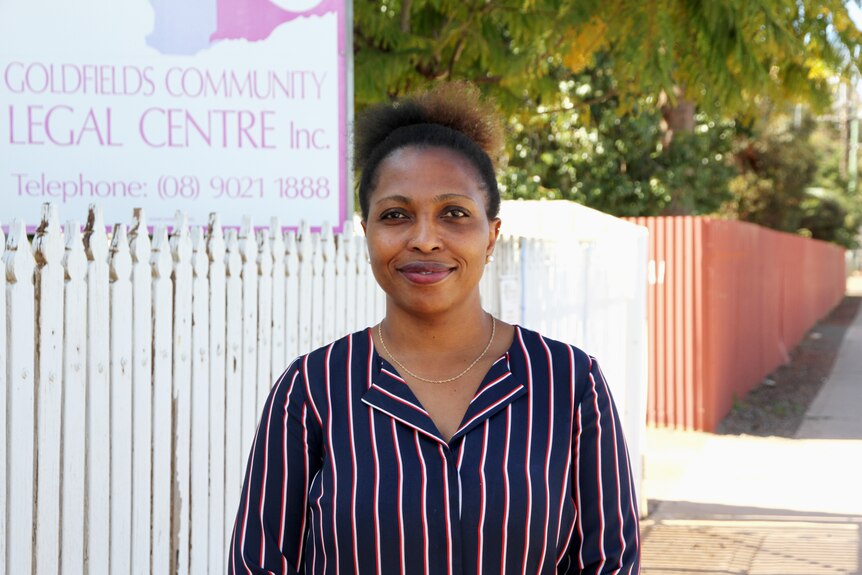 A woman stands smiling out the front of a community legal centre.
