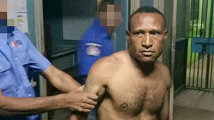 A photo of Andy Paro in police custody. He is not wearing a shirt, and a police officer is holding him by the arm.