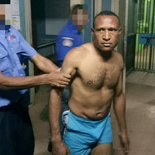 A photo of Andy Paro in police custody. He is not wearing a shirt, and a police officer is holding him by the arm.