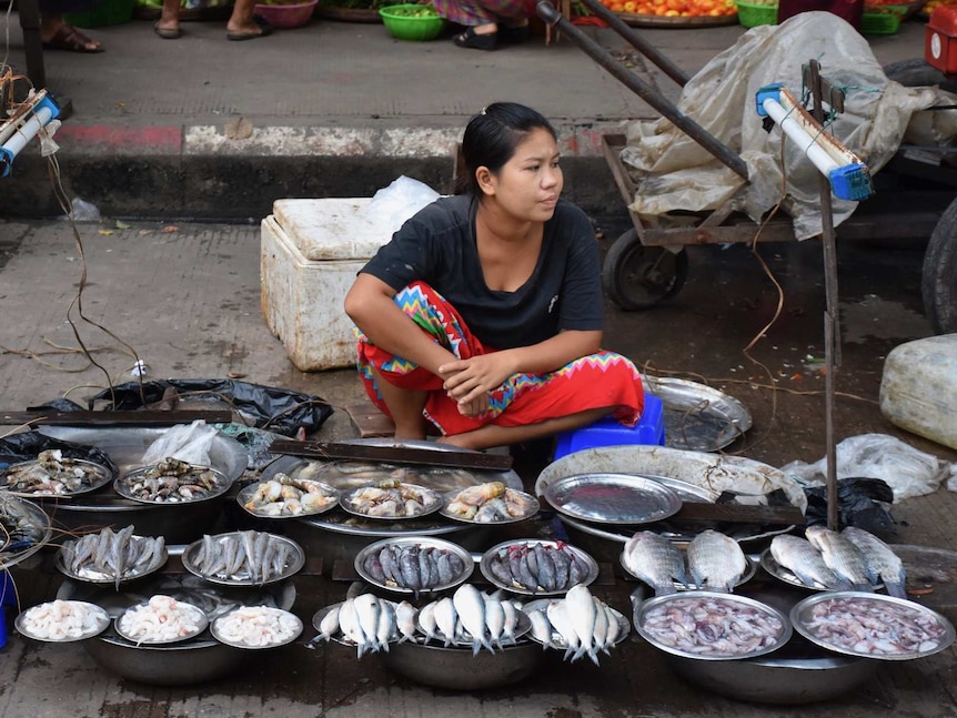 A woman sits on the footpath in Myanmar selling fish