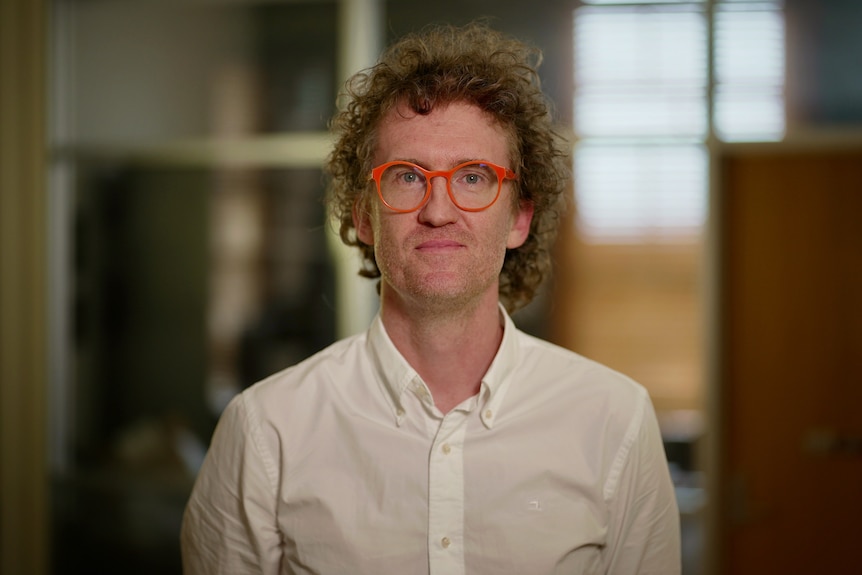 A profile image of a man with curly hair, wearing a white shirt and orange glasses.