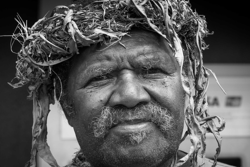 A close-up, black and white photo of the face of a man wearing a headdress.