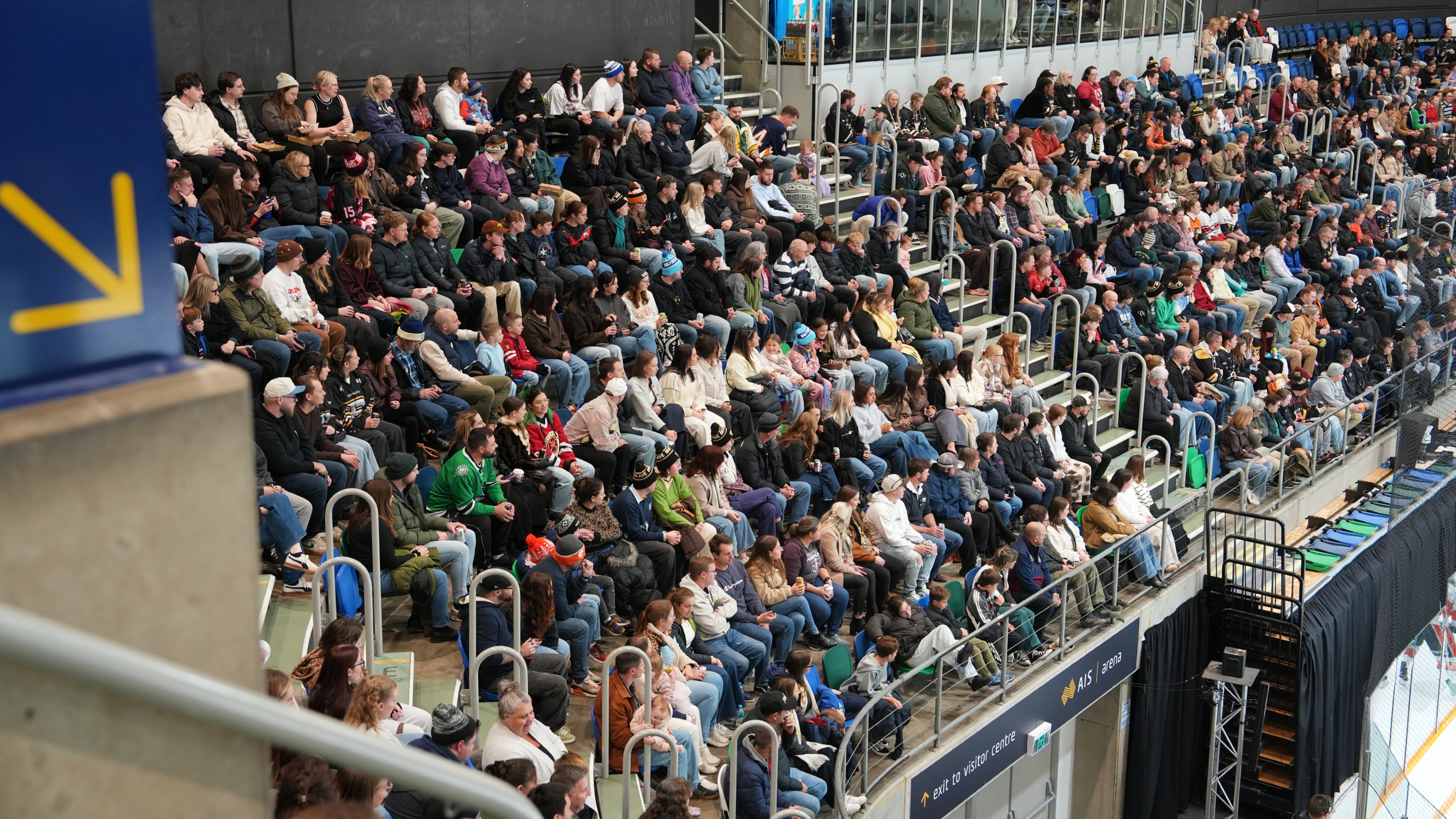 A crowd of people sit in the stand watching the rink.