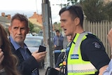 Philip Whiteman on a suburban street holding a phone, standing opposite a police officer.