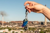A male hand holds a set of keys in front of the Mount Isa skyline. The town and mine is in the background.