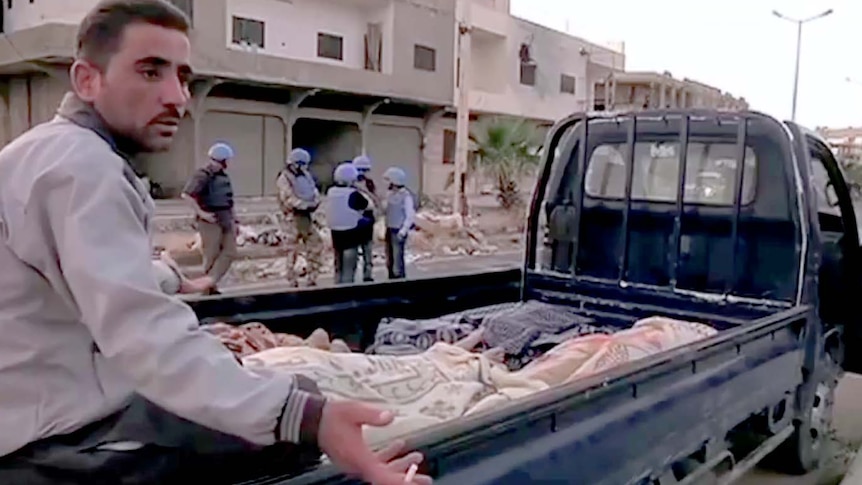 A man sits on the back of a ute with bodies from a massacre in the town of Houla