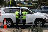 Two police in high visibility yellow vests speak to a person inside a white car