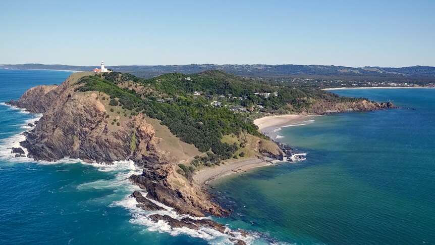 An aerial shot of a coastline with a lighthouse on top of the hill