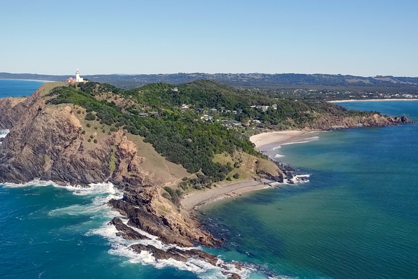 An aerial shot of a coastline with a lighthouse on top of the hill