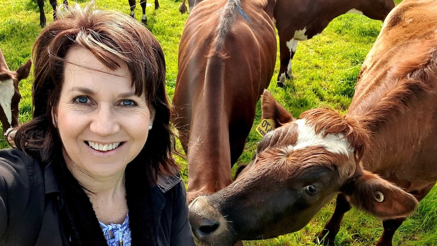 A brown haired woman takes a selfie with a herd of cattle