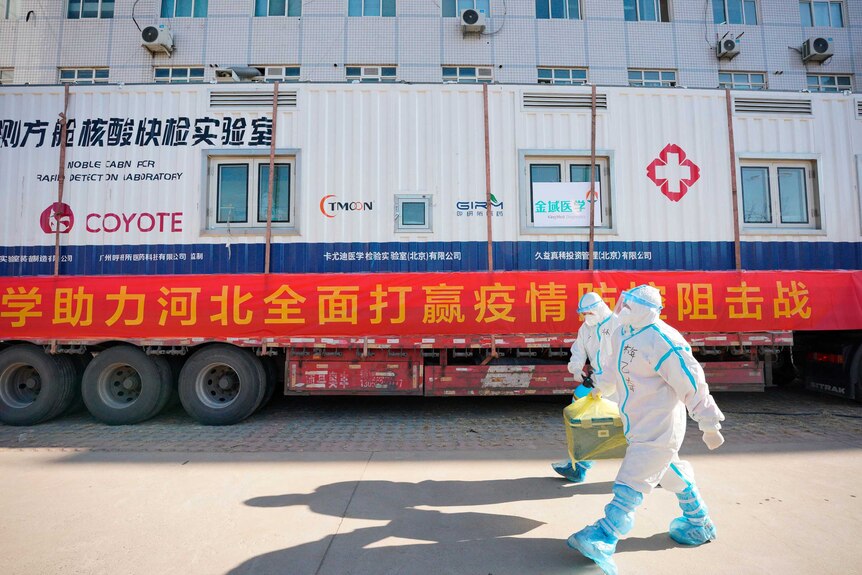 Two workers carry a container of coronavirus test samples outside of a residential neighbourhood in Shijiazhuang.