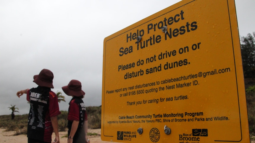 Two kids point away from sign on Cable Beach. 