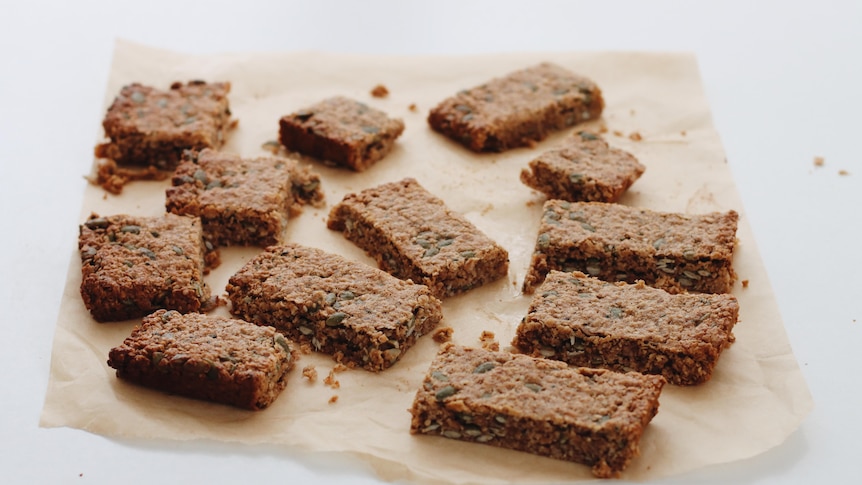 Rectangular pieces of a muesli bar slice sit randomly spaced on a piece of baking paper.