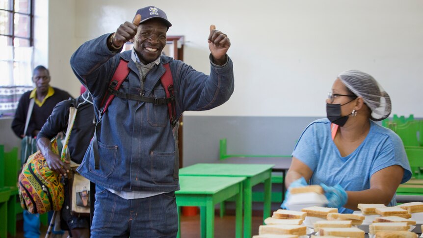 A man gives a double thumbs up before accepting lunch from a staff member at a soup kitchen