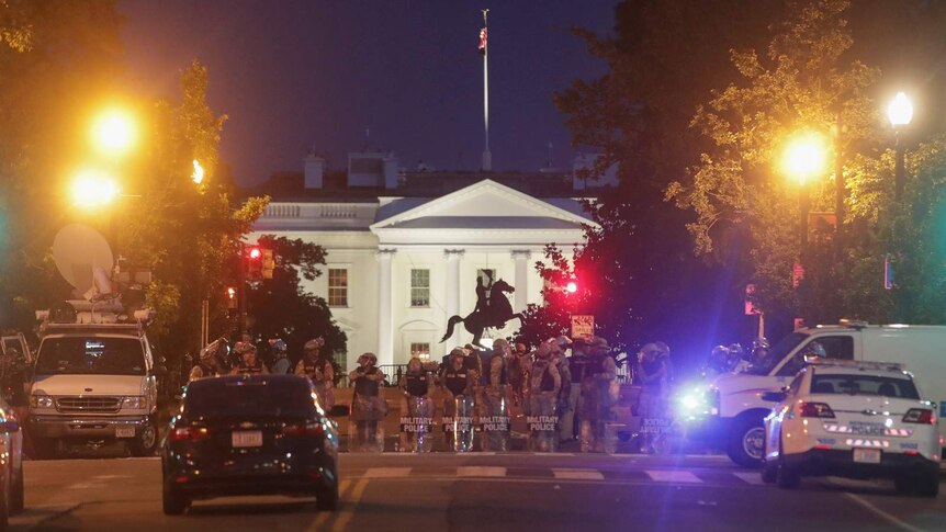 Military police stand in front of the White House at night.