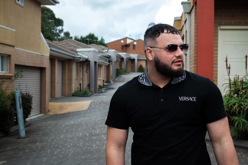 A man wearing sunglasses stands outside a row of townhouses.