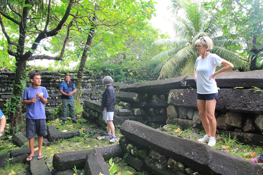 Julie Bishop at Nam Madol ruins, stands surveying basalt stones in a tree covered area.