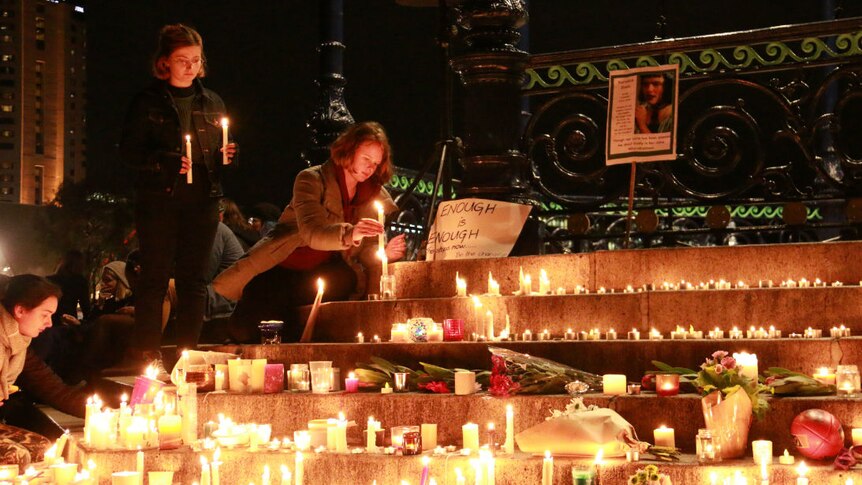 Women place candles at a vigil for Eurydice Dixon, being held in Adelaide.