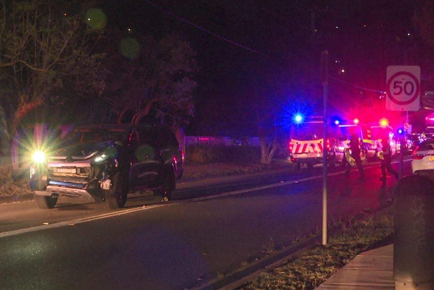 A dented car in front of ambulances on a dark street