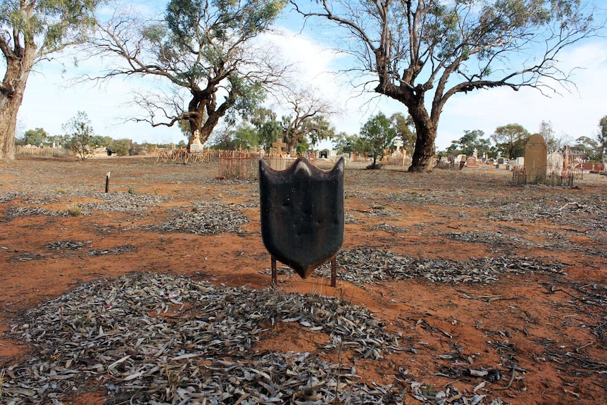 An unknown grave marked by a black shield shape marker in a bush landscape.