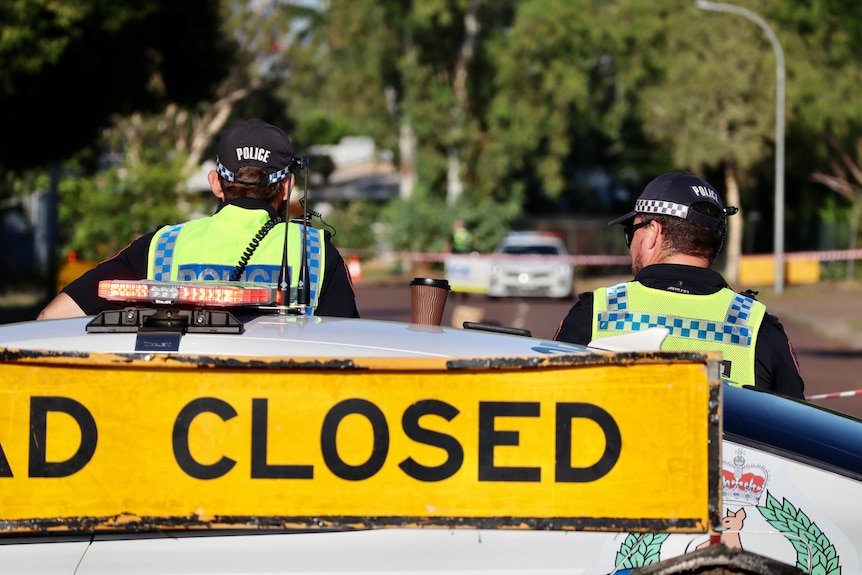 A neon yellow sign reads 'closed' ahead of two police officers facing away from the camera. 