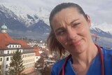 A woman wearing scrubs and a stethoscope posses in front of the Alps