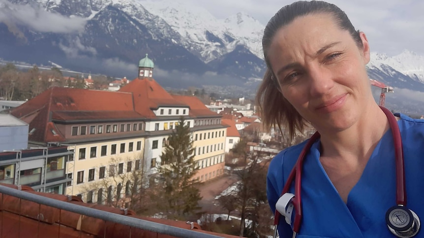 A woman wearing scrubs and a stethoscope posses in front of the Alps