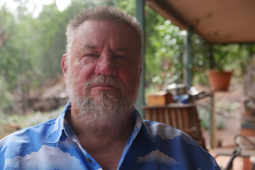 Katherine's former GP Peter John Spafford is sitting on his verandah in Katherine with contaminated bushland in the background.