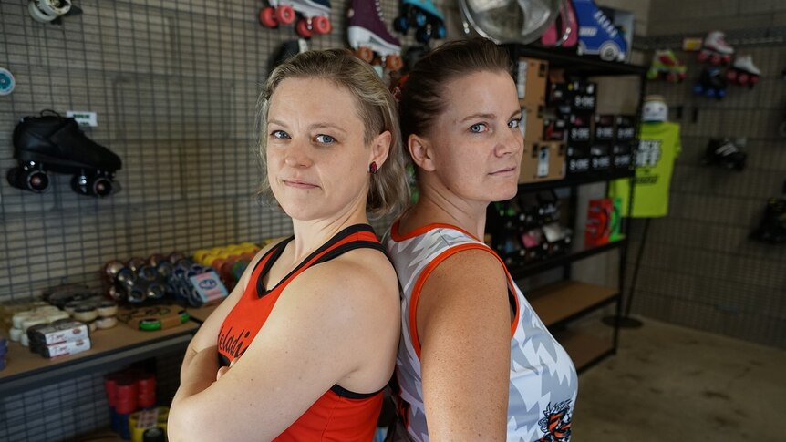 Two women stand back-to-back in a skating shop.