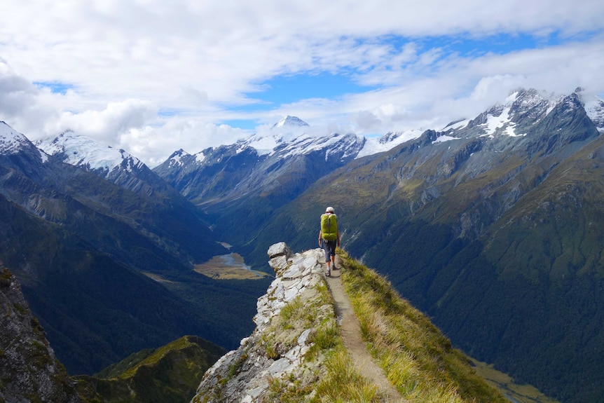 A woman with a large backpack on looks out over beautiful mountain scenery.