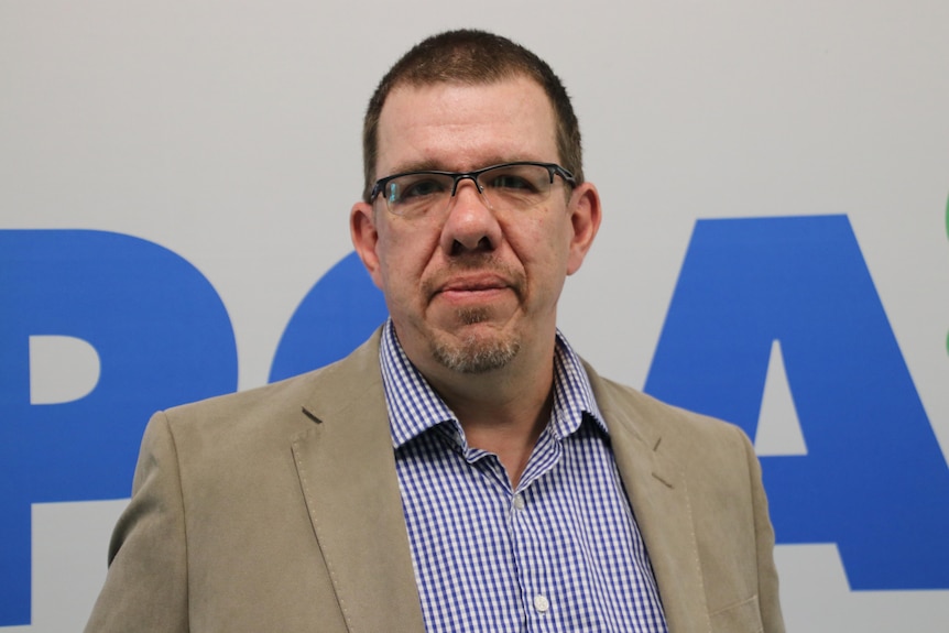 A mid-shot of RSPCA WA chief executive Ben Cave posing for a photo indoors in a suit jacket and checked shirt.