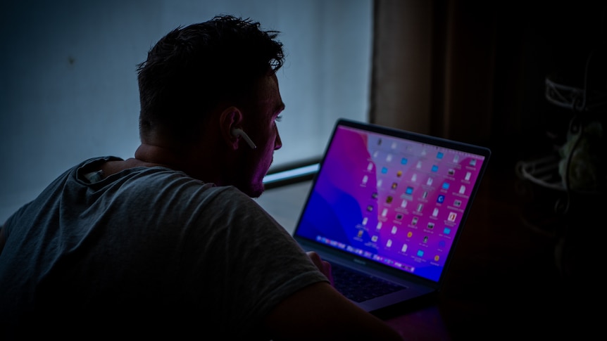 An unidentifiable man looking at a computer screen