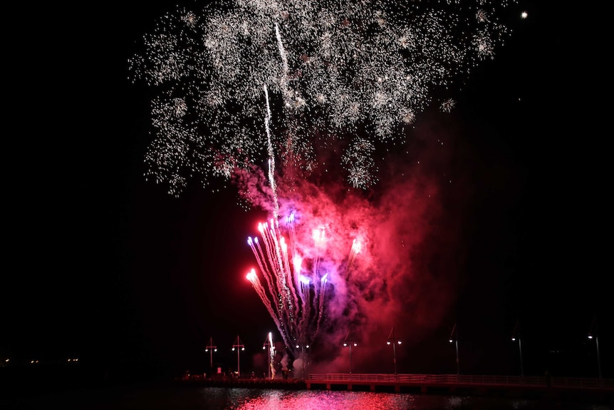 Fireworks: Streams of red light streak up into the black sky beneath a large burst of gold specks.